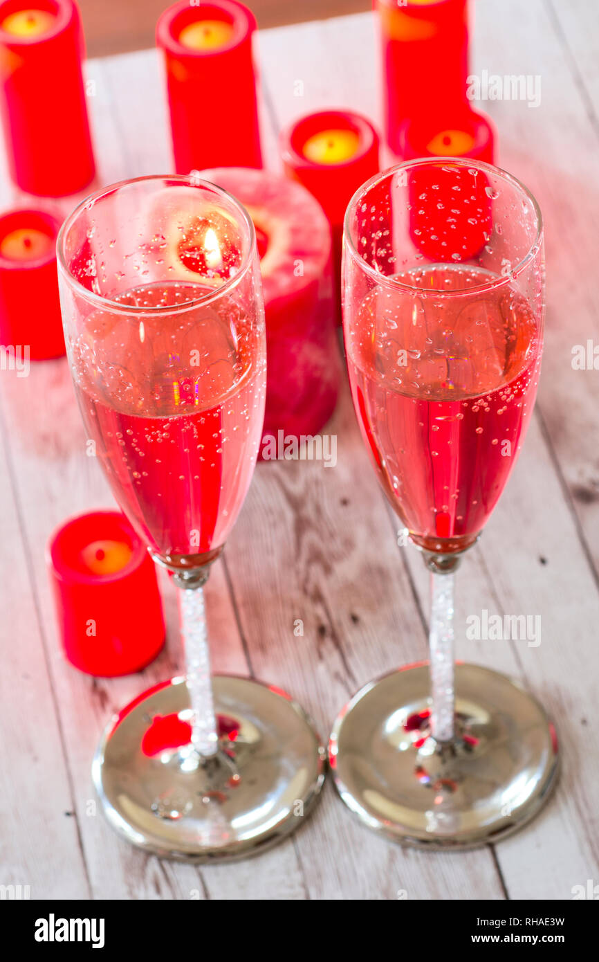 Two champagne flutes filled with pink bubbly beverage, on the tabletop surrounded with burning red candles. Stock Photo