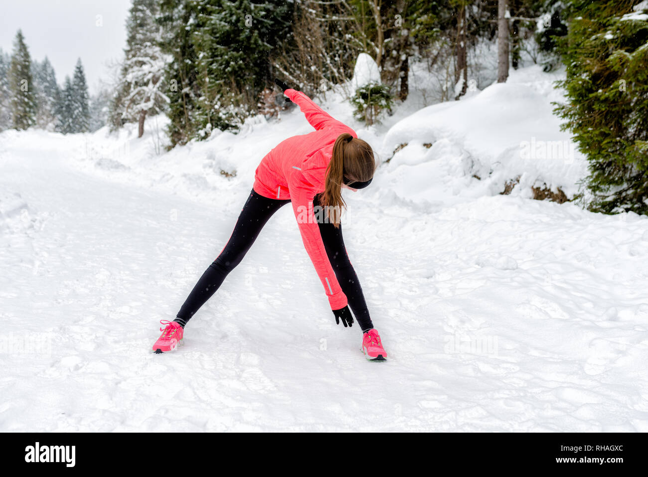 Young sport woman doing exercises during winter training outside in winter mountains wearing warm clothing gloves in snow weather Stock Photo