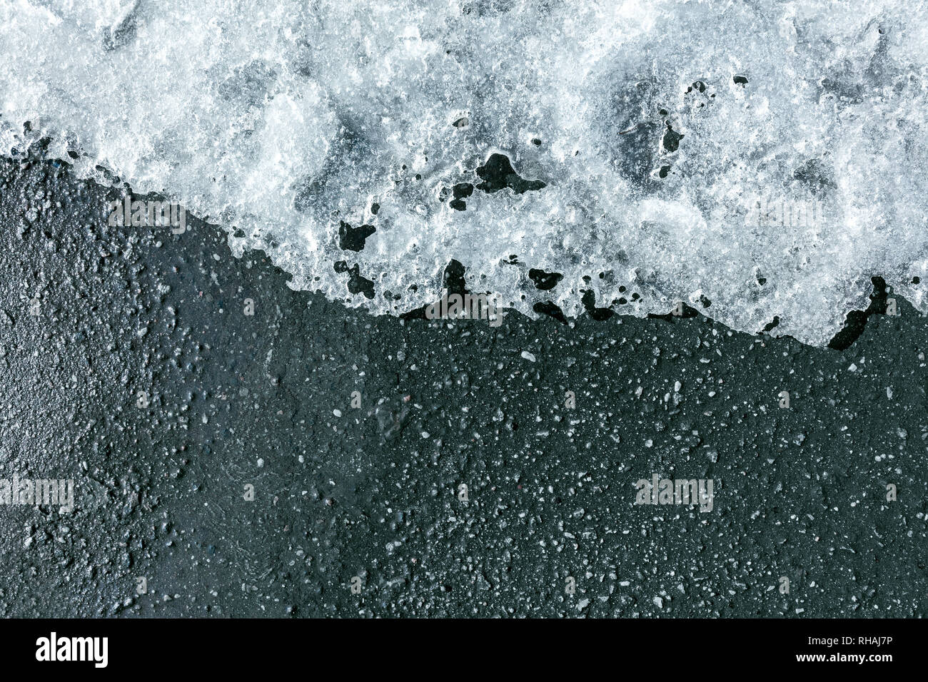 ice melting on black asphalt or pavement. thawing snow on the sidewalk