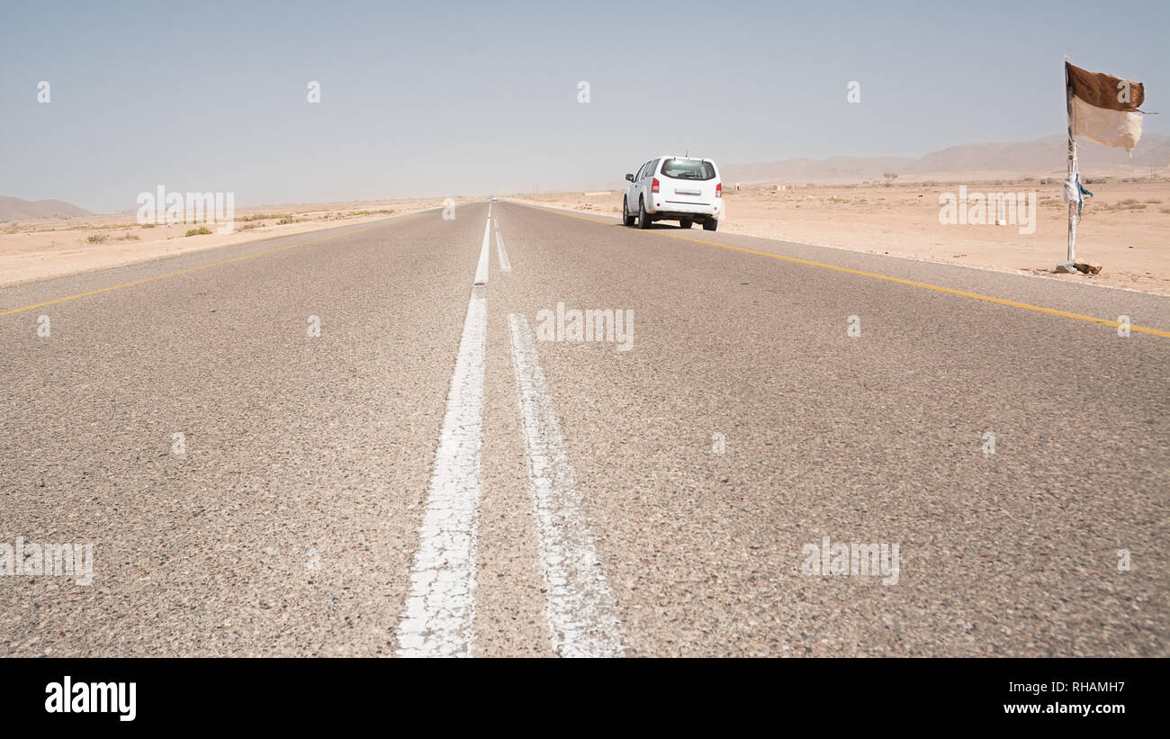 Asphalt road straight in the desert in the south of Oman with a parked 4x4 vehicle Stock Photo