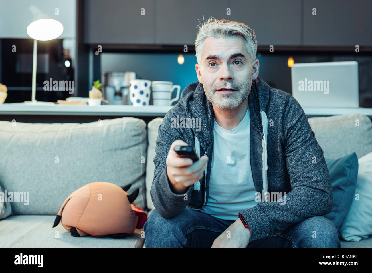 Grey-haired bearded attractive man in sportswear watching tv Stock Photo