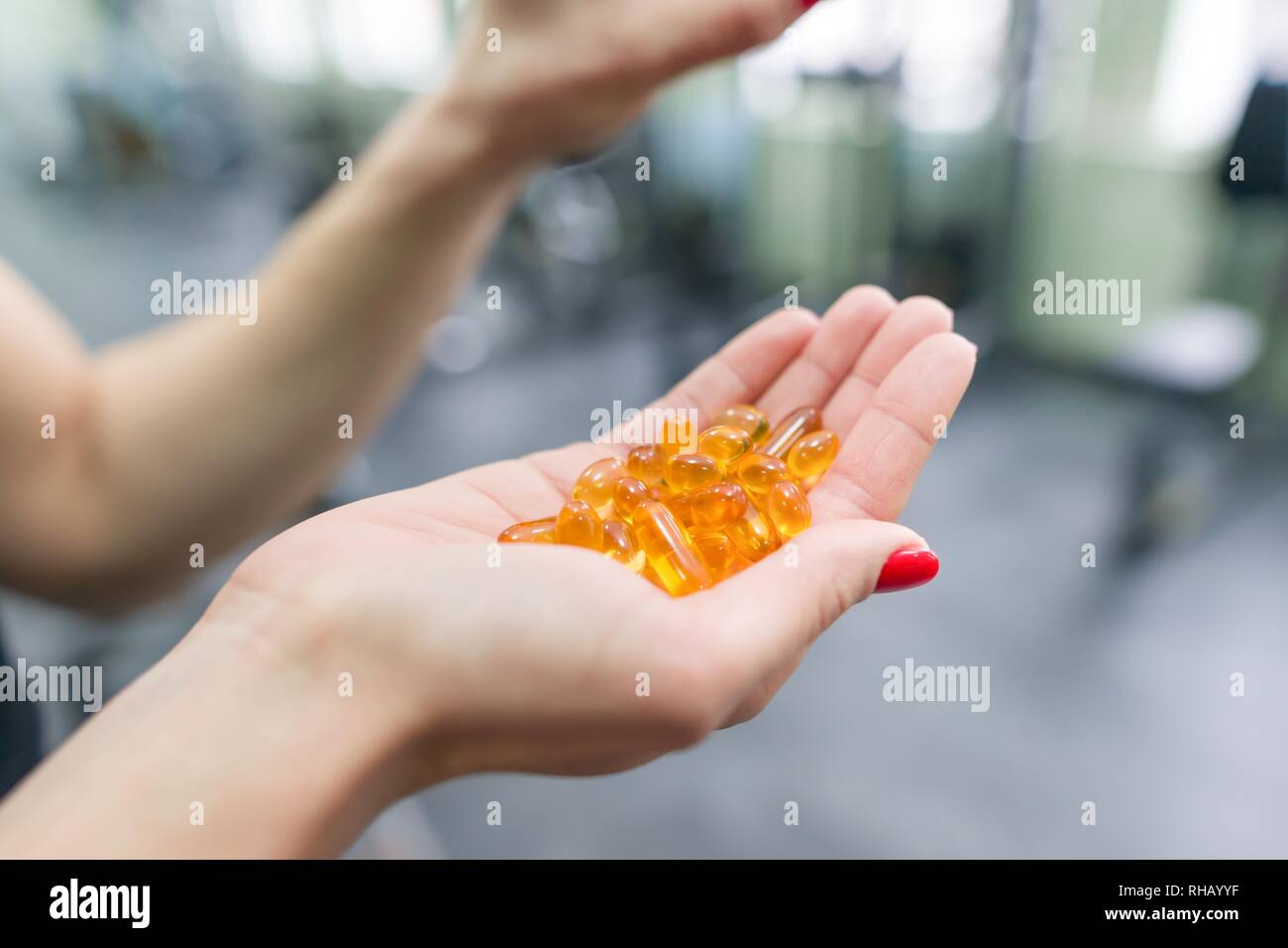 Closeup of fitness woman hands showing vitamin e capsule omega-3, gym background. Healthy lifestyle, medicine, nutritional supplements and people conc Stock Photo