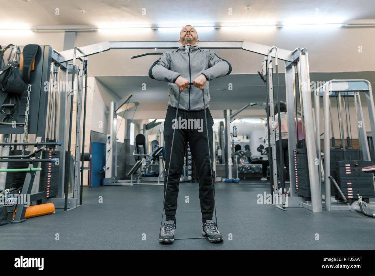 Senior man doing muscle recovery exercises sitting on a swiss ball in front  of the tablet. Old person pensioner online internet exercise training at  home sport activity with dumbbell, resistance band, swiss