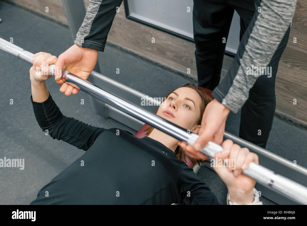 Male personal fitness trainer helping young woman to do workout in gym ...