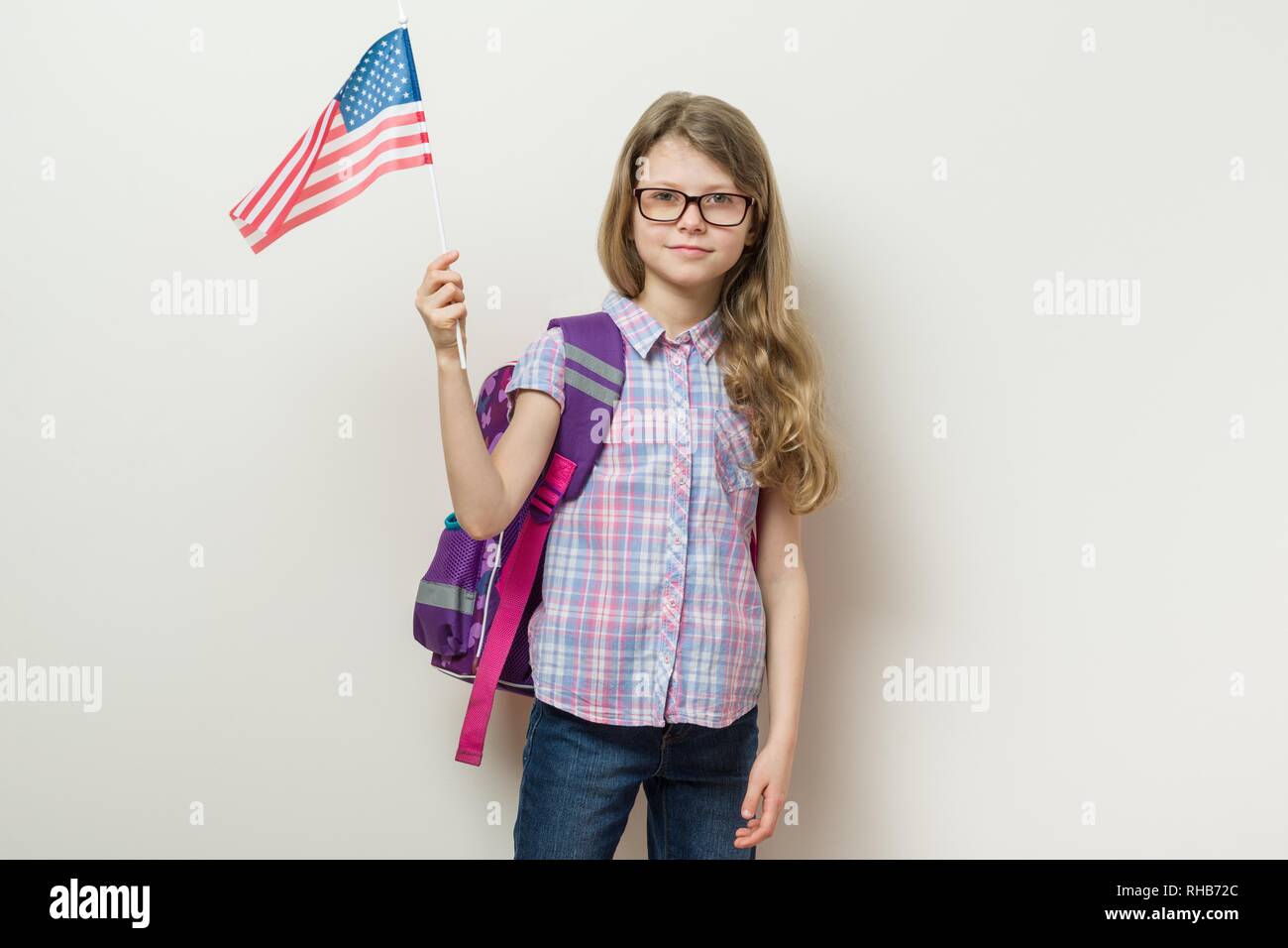 School child with a backpack holds the USA flag, background bright wall in the school. Stock Photo