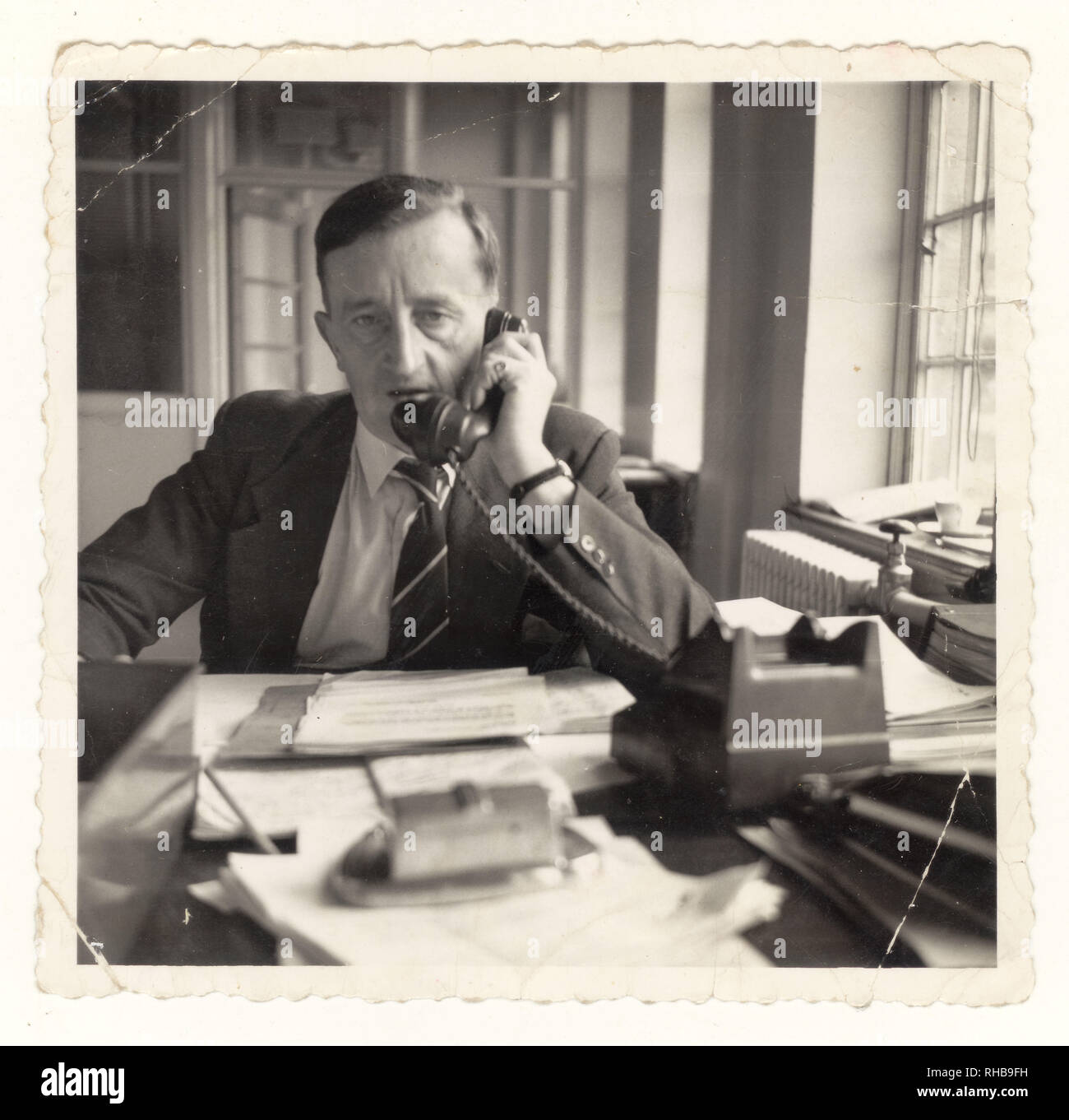 Photo of stressed unhappy older middle aged man, management, manager, managing / working in office using telephone circa 1950's, U.K. Stock Photo