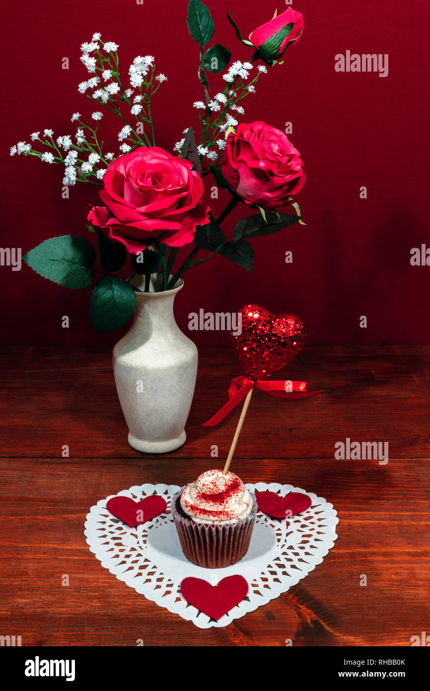 Beautiful pink roses in a vase accented with Baby's Breath flowers, heart shaped white dollie with a decorated cup cake with a heart on a pick. Stock Photo