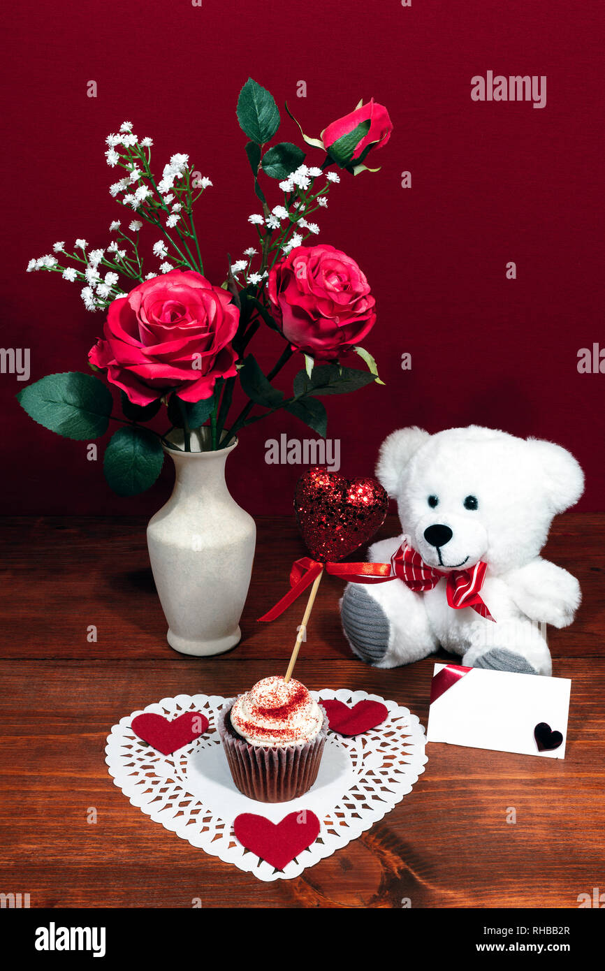 Beautiful pink roses in a vase accented with Baby's Breath flowers, heart shaped white dollie with a decorated cup cake with a heart on a pick. A whit Stock Photo