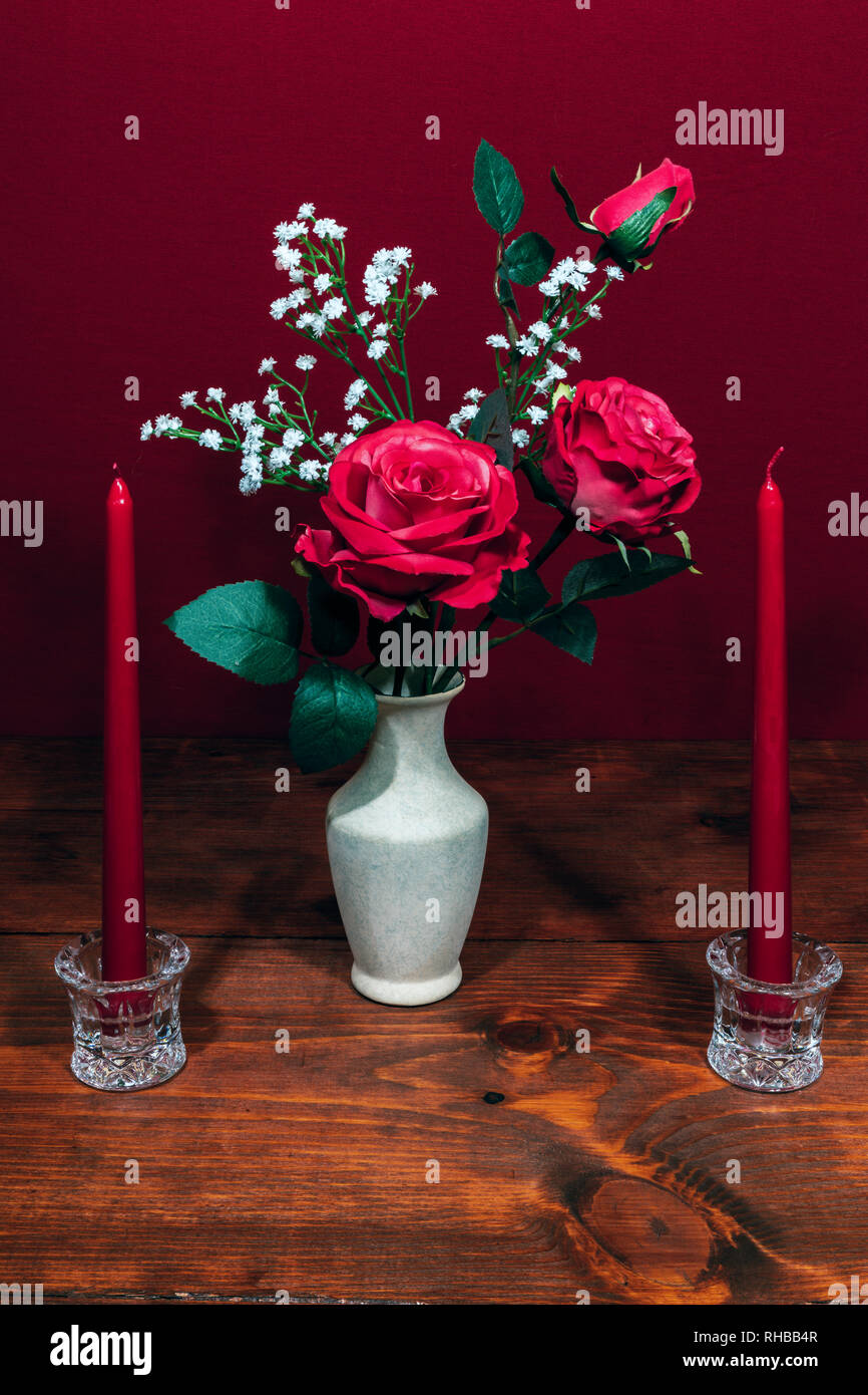 Beautiful pink roses in a vase acsented with Baby's Breath flowers, Two red candles in crystal holder. Stock Photo