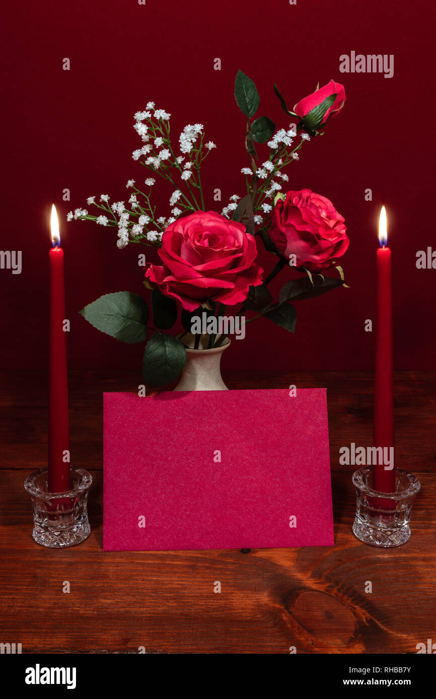 Beautiful pink roses in a vase accented with Baby's Breath flowers, Two lit ed candles in crystal holder and a card Stock Photo