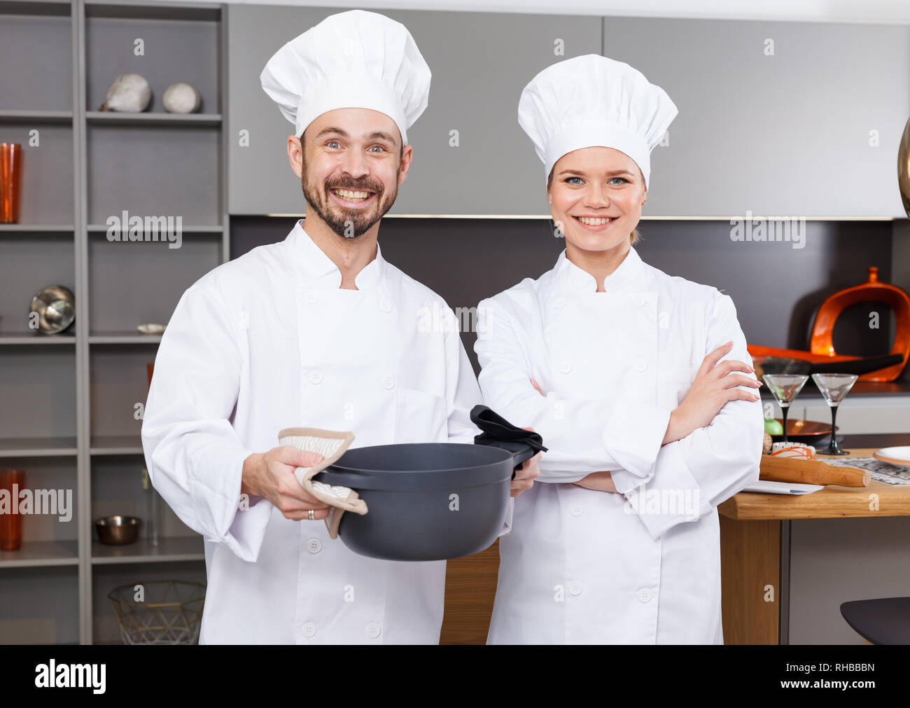 Two confident personal chefs in white coats standing in modern interior of private kitchen Stock Photo