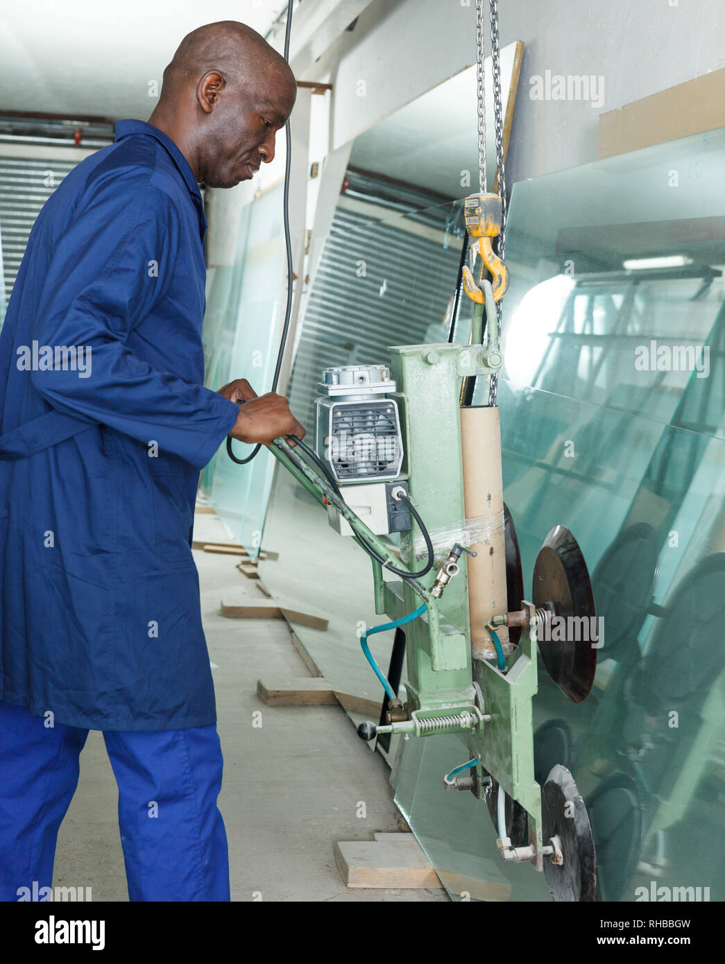 Focused AfricanAmerican worker using vacuum glass lifter for sheet