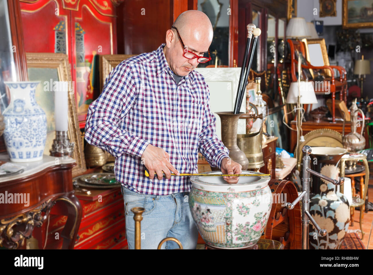 Middle aged man working in antique store, measuring vintage vase with tape rule Stock Photo