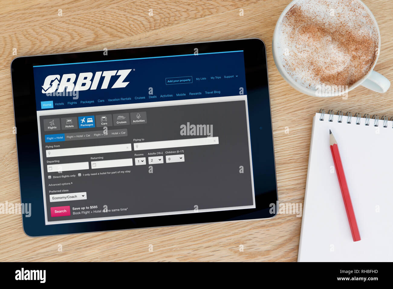 The Orbitz website features on an iPad tablet device which rests on a wooden table beside a notepad (Editorial use only). Stock Photo