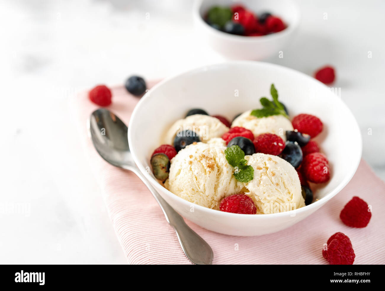 Vanilla ice cream balls in a bowl on hwite table with berries. Close up ...