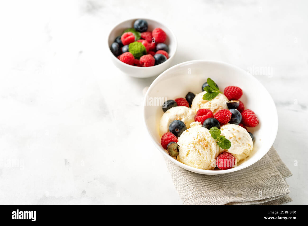 Vanilla ice cream balls in a bowl on hwite table with berries. Copy space Stock Photo