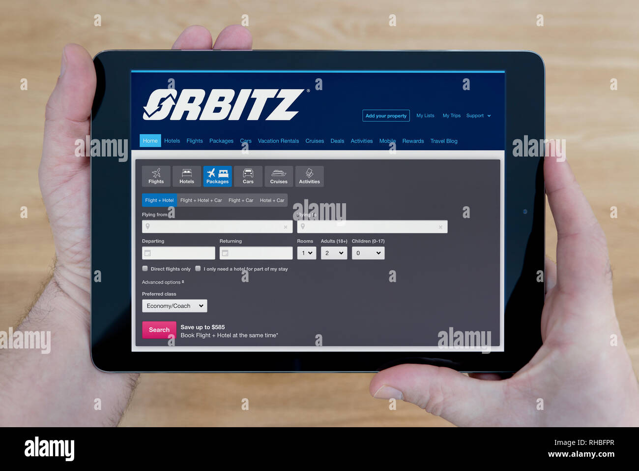 A man looks at the Orbitz website on his iPad tablet device, shot against a wooden table top background (Editorial use only). Stock Photo
