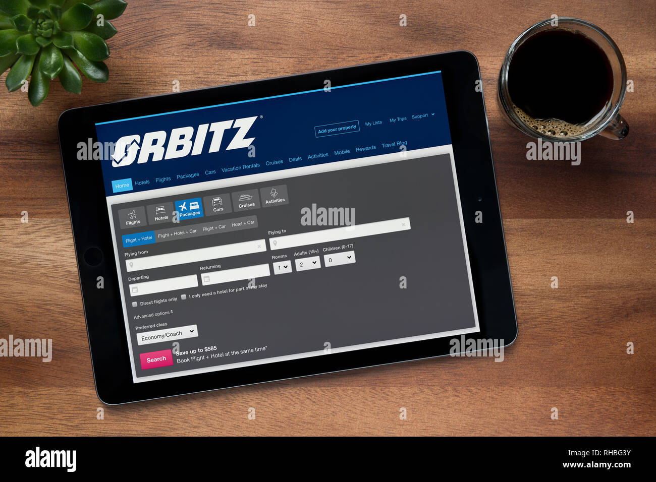 The website of Orbitz is seen on an iPad tablet, on a wooden table along with an espresso coffee and a house plant (Editorial use only). Stock Photo