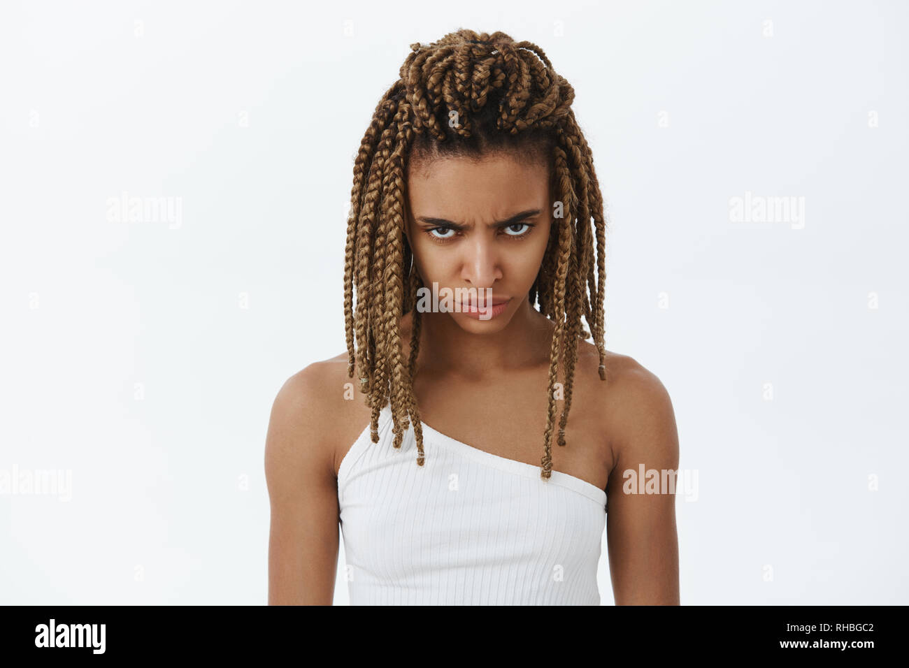 Waist-up shot og angry and moody displeased hateful dark-skinned young female with dreads looking from under forehead with scorn and hate looking Stock Photo