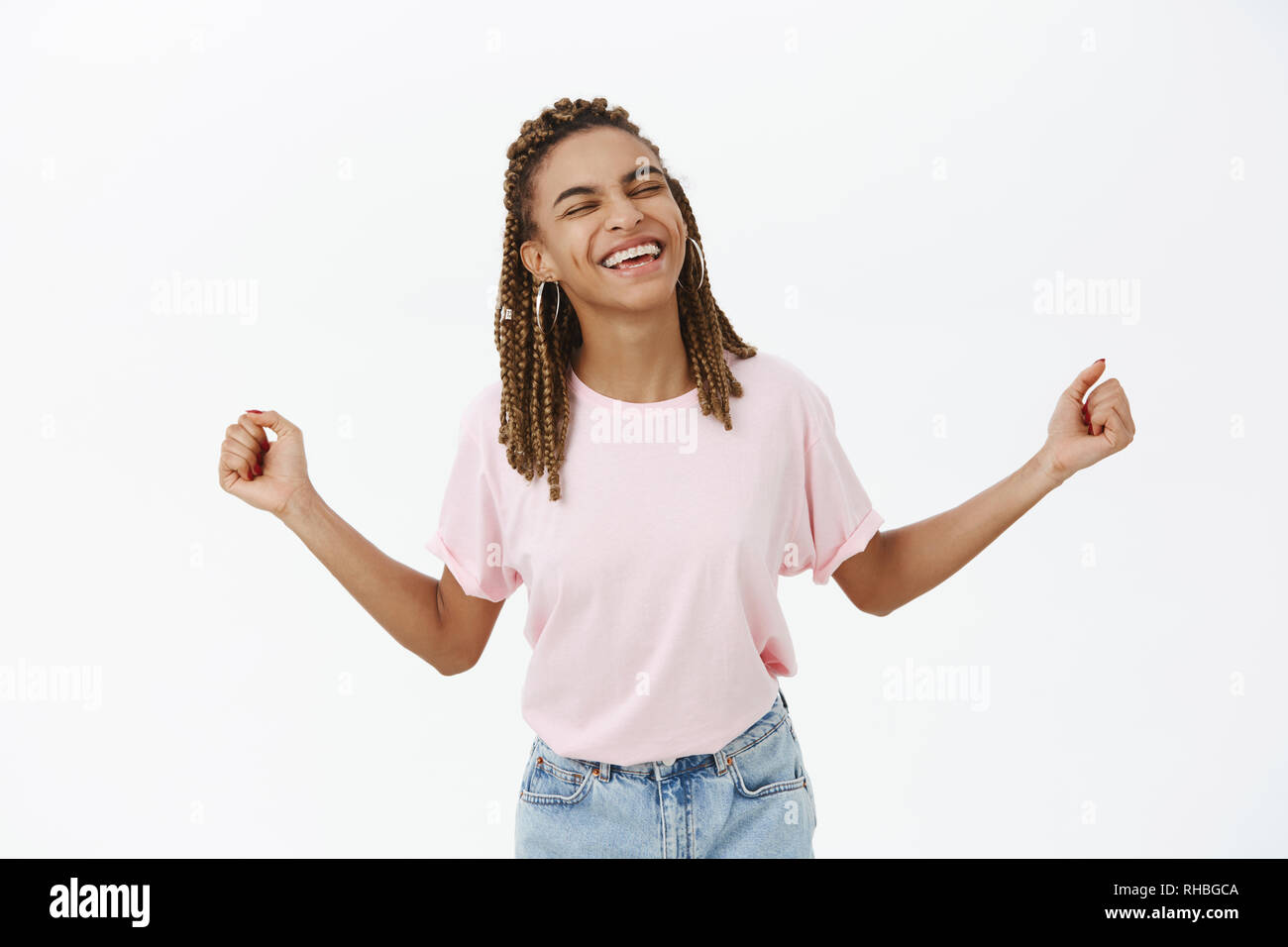 Yeah baby I am super. Joyful happy and triumphing lucky and successful young female designer with dreadlocks in pink t-shrt spreading hands aside Stock Photo