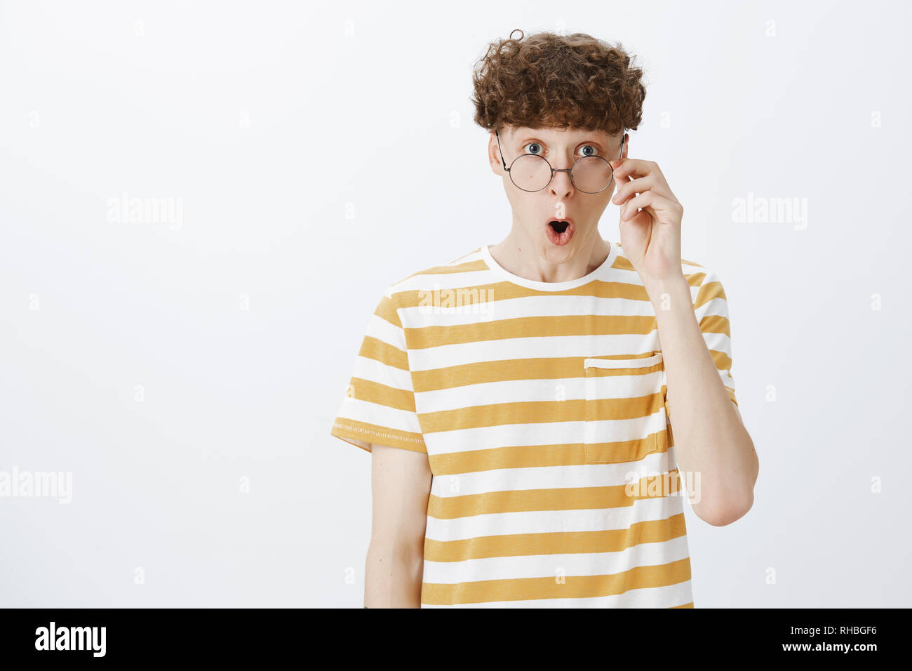 Amazed and amused funny guy with curly hairstyle and tattoo dropping jaw yelling wow and taking off glasses as being amazed and speechless seing Stock Photo