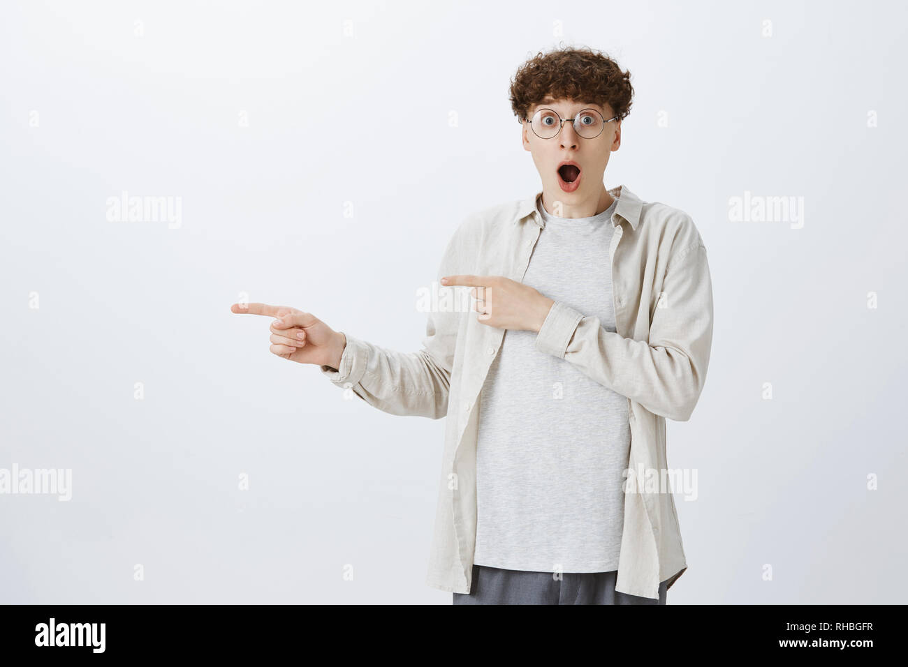 No way it real. Portrait of amazed young teenage guy in round glasses with curly hair losing speech from amazing low prices dropping jaw staring Stock Photo