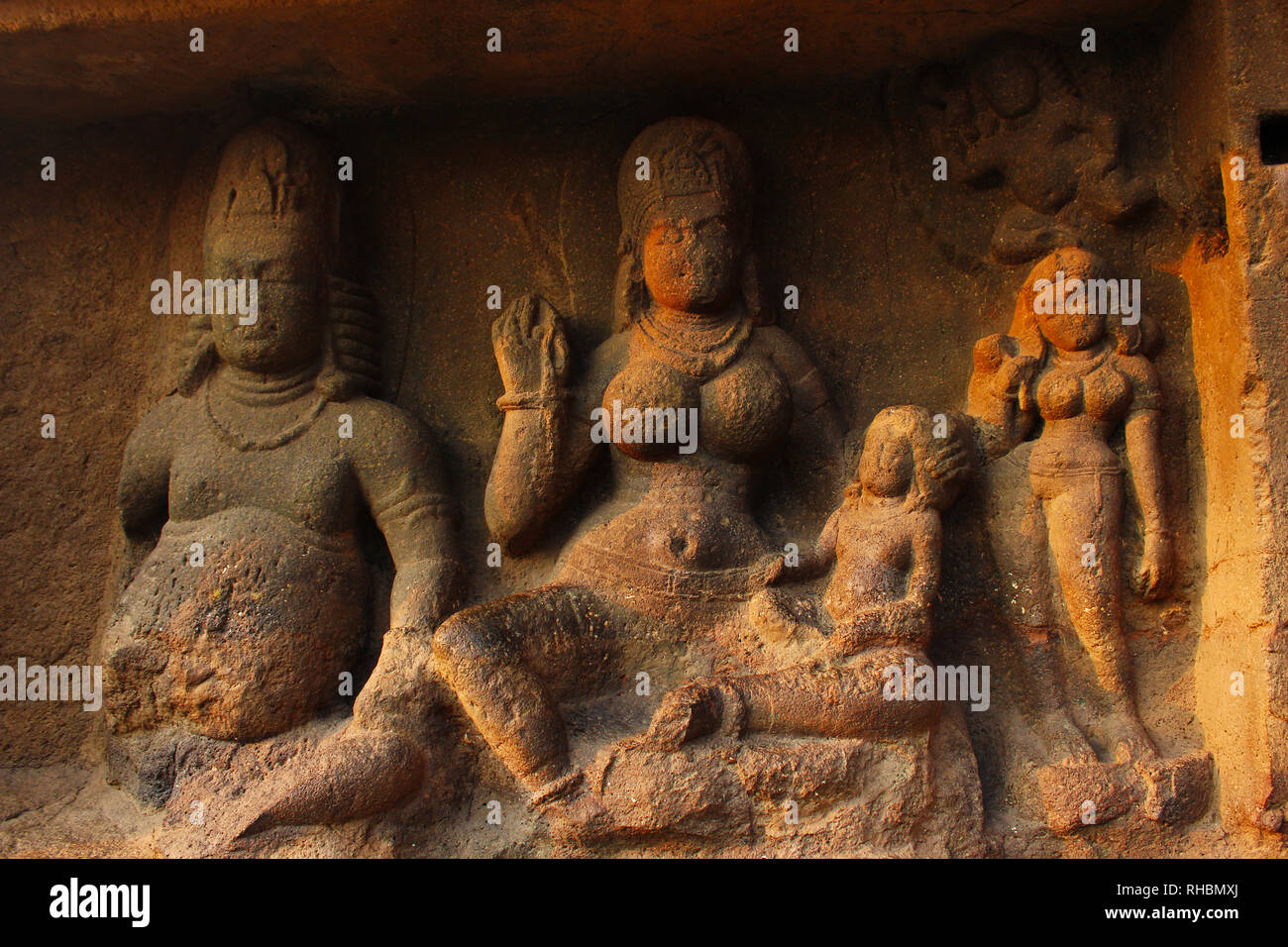 Yaksha Jambhala sits with his wife, Hariti, who holds one of her five hundred children on her lap, Cave 8, Ellora Caves, Aurangabad, Maharashtra Stock Photo