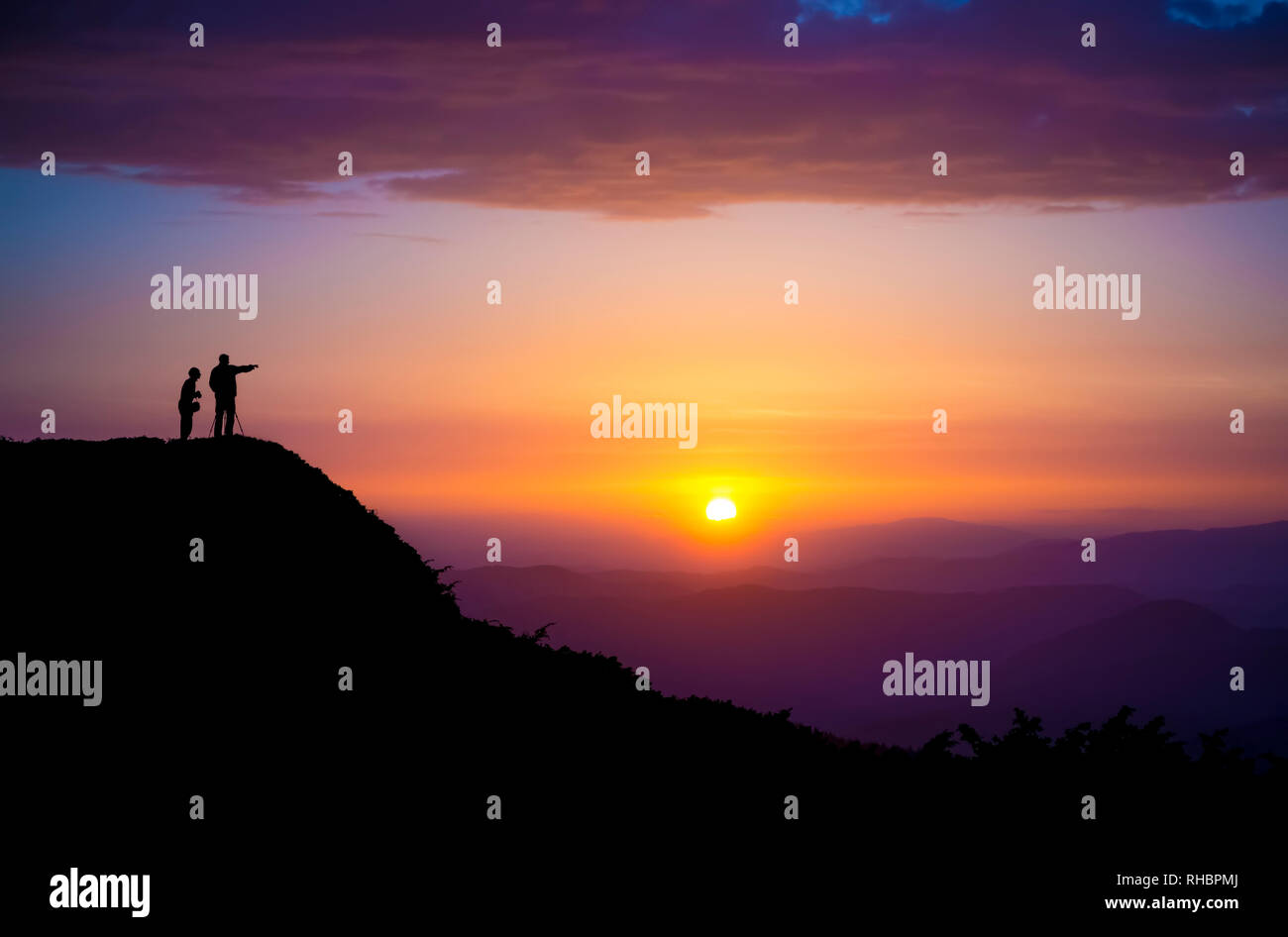 Evening landscape. Silhouettes of two people standing on a rock and looking toward the sun. Sunset in the mountains. Purple light. Summer in the Ukrai Stock Photo