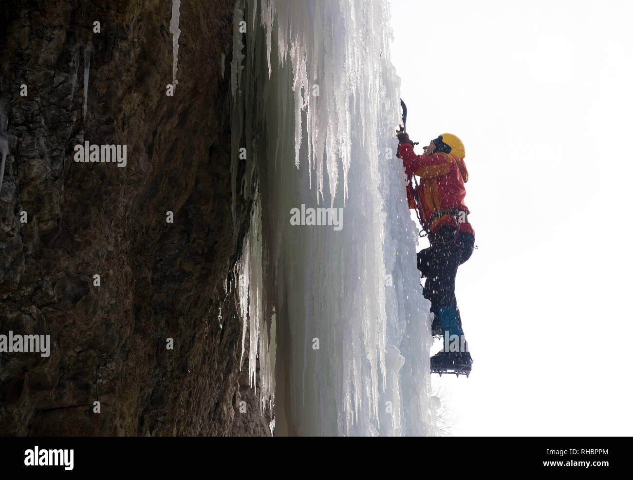 Extreme ice climbing. Man climbing the frozen waterfall using ice axes