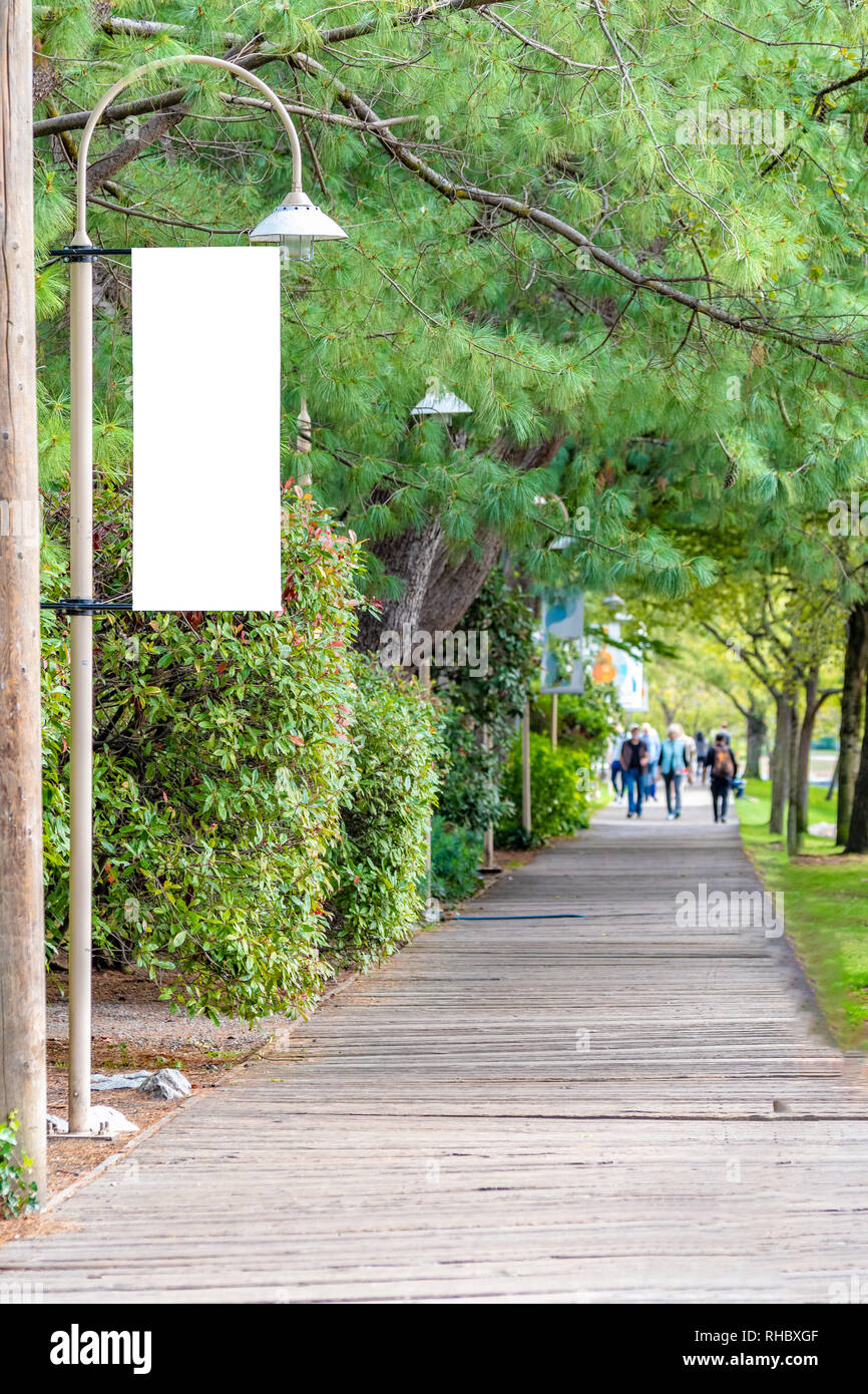 Download Blank White Isolated Vertical Banner Flag Mockup Signage Sign On A Streetlight Public City Park Walkway Unrecognizable People Walking In Distance Stock Photo Alamy