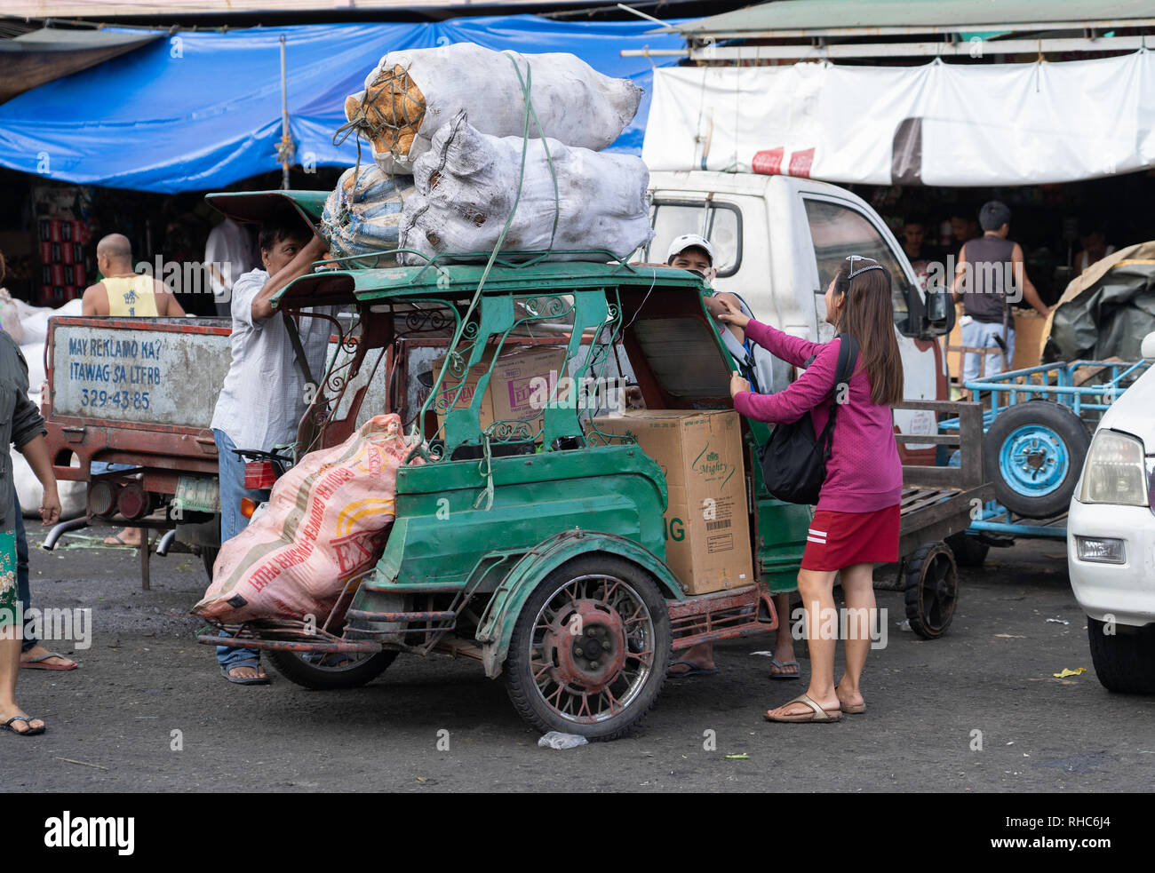 A vehicle known as a tricycle in the Philippines,a combination of motorcycle and sidecar, being loaded with market produce Stock Photo