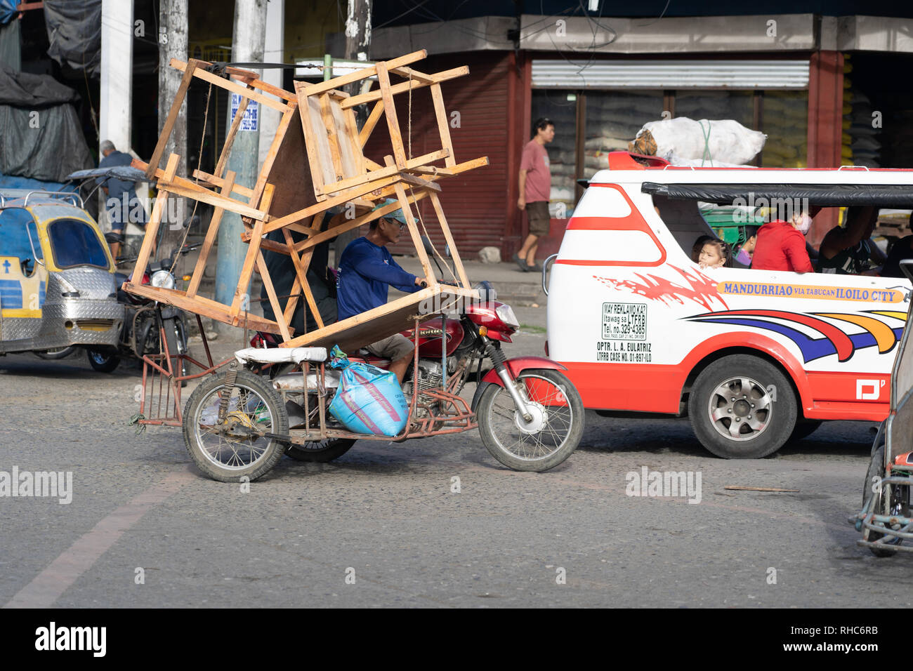 A Tricycle vehicle overloaded with what appears to be wooden tables. Stock Photo