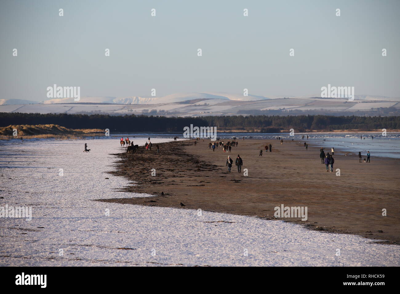 St Andrews, UK. 2nd February 2019. People walking on West Sands beach St Andrews after overnight snow with distant snow covered peaks in the Angus Glens.  © Stephen Finn/Alamy Live News Stock Photo