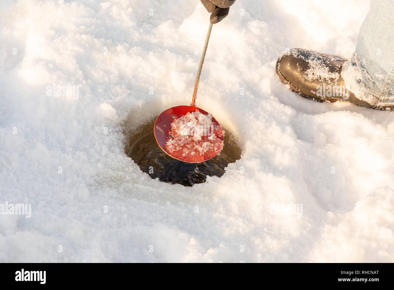 Clearing the ice fishing hole with a homemade ice scooper. Stock Photo