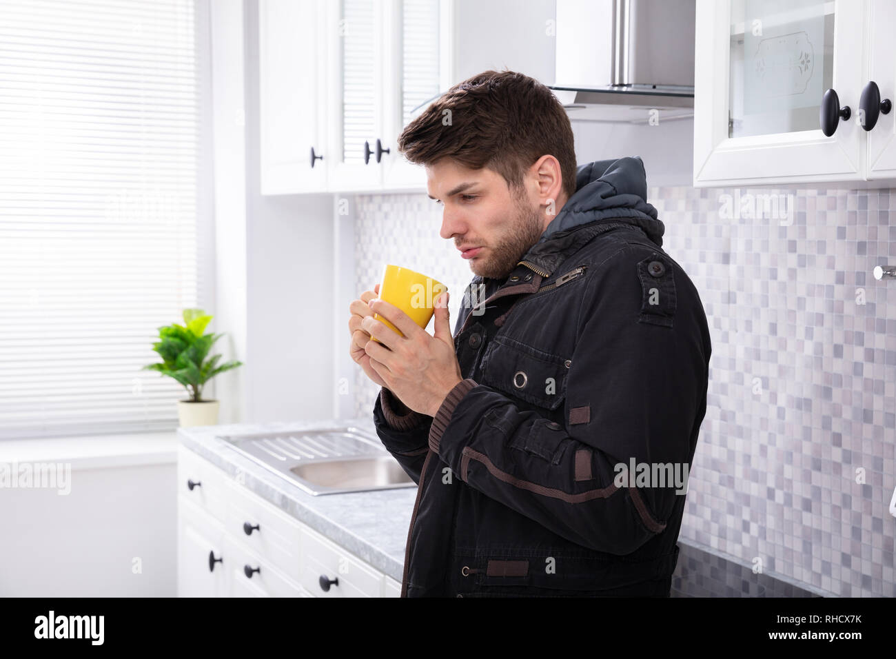 Side View Of Sick Man Drinking Coffee Standing In Kitchen Stock Photo