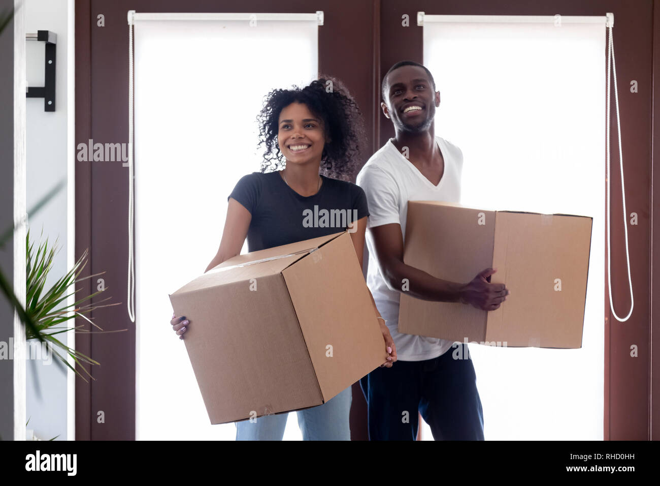 Excited black couple carrying boxes entering big modern house hallway Stock Photo