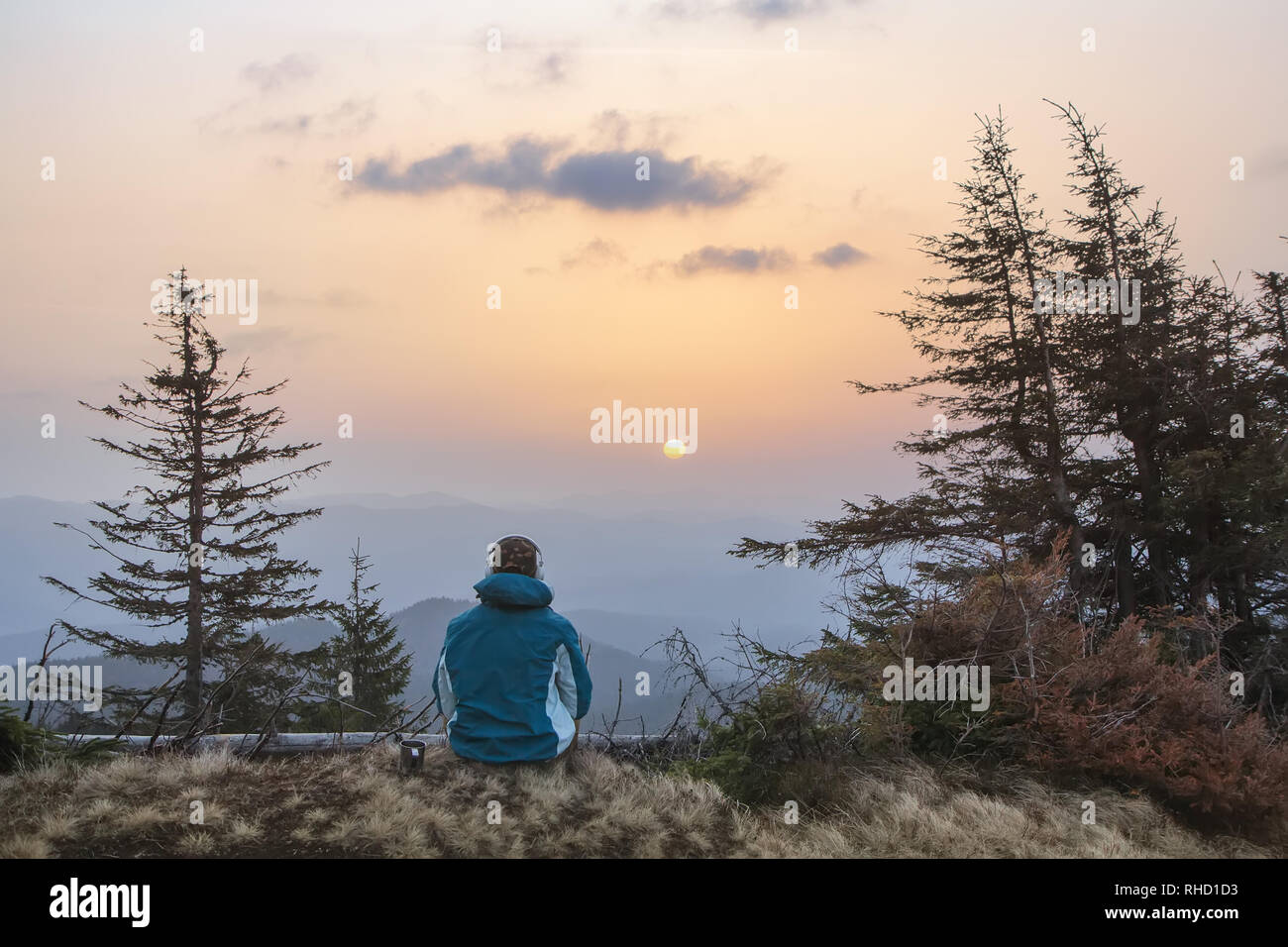 A young youth in headphones watches the sunrise in the mountains with a cup of tea, a sonception, a trip, a hike, a rest, solitude Stock Photo