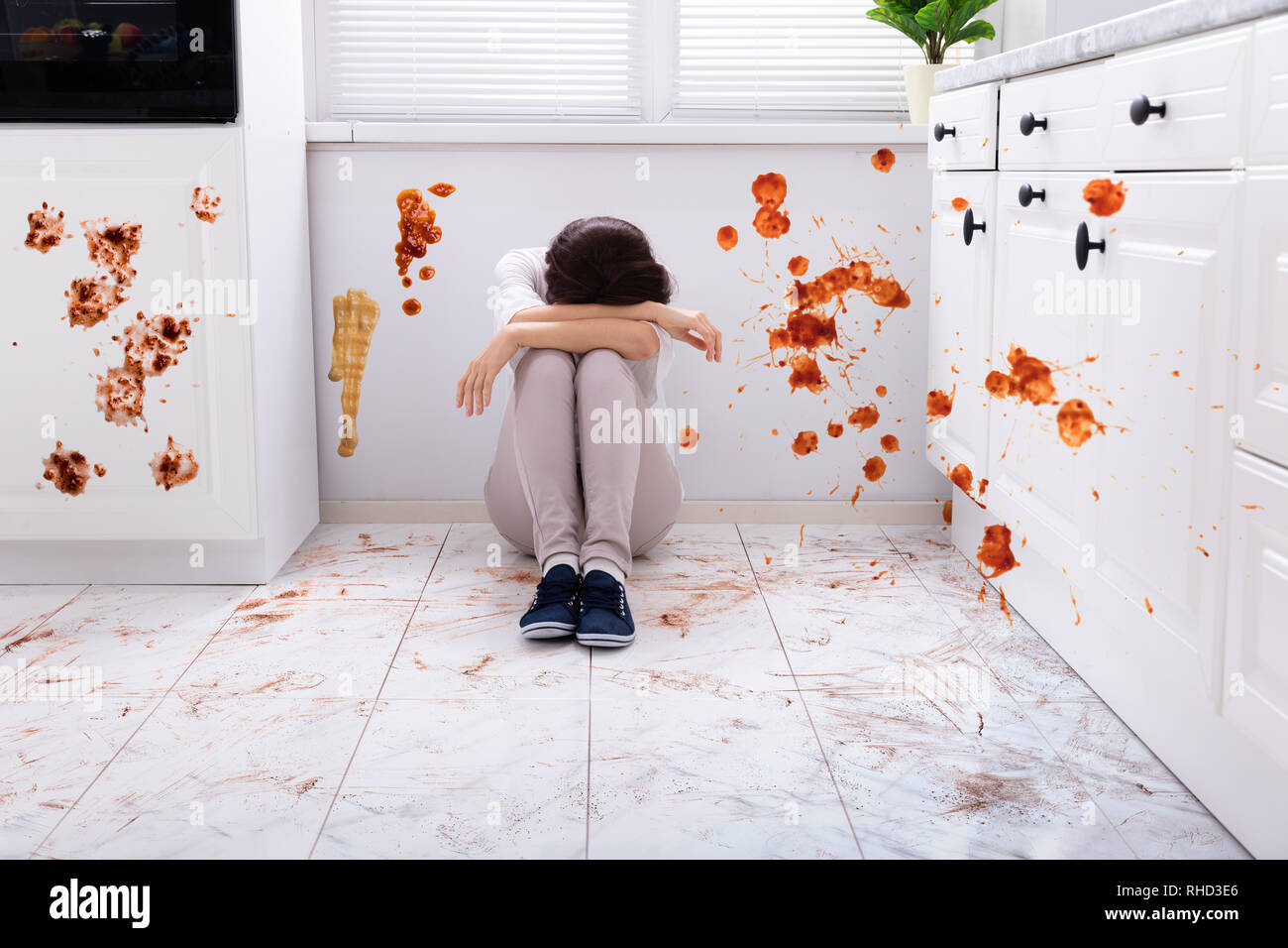 Sad Woman Sitting On Floor With Spilled Food In Kitchen Stock Photo - Alamy