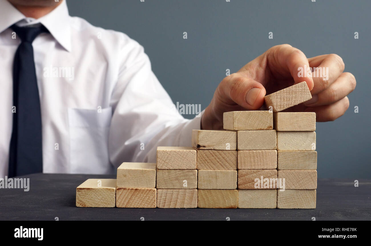 Success in business and career. Man rises figurine on a ladder from wooden blocks. Achievement. Stock Photo