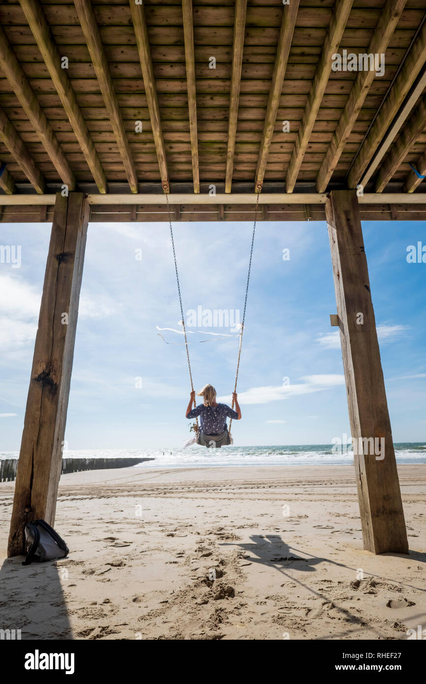 woman sitting in a decorated swing on the beach overlooking the sea on a sunny day with a blue sky Stock Photo