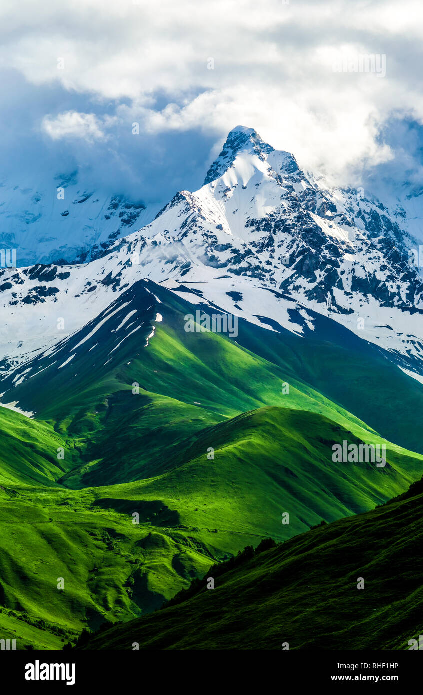 Beautiful view of the snowy mountain peak. Green fields and hills changes  to snow. Storm white clouds are visible behind the lighted mountain top.  Sum Stock Photo - Alamy