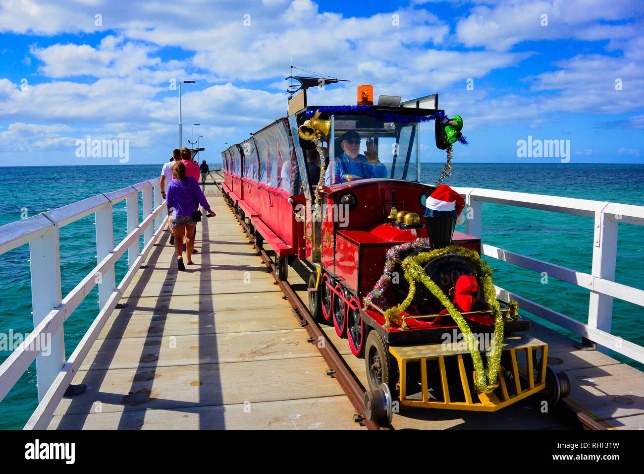 Colorful shot of surprising vision of christmas decorated train on famous Busselton Jetty, Western Australia, driven by a Santa Claus looking old man. Stock Photo