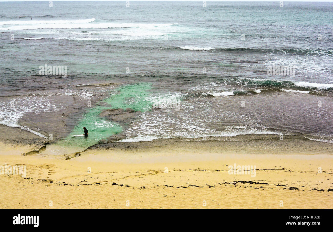 Surfer entering the ocean in a river mouth, between rocks and corals