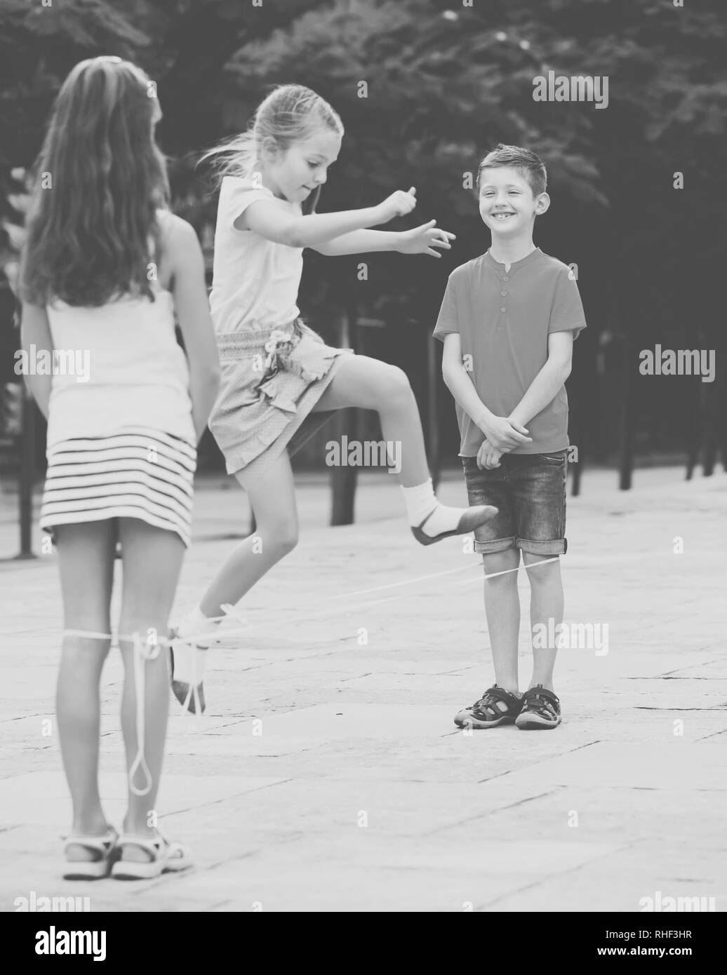Kids in school age playing together with chinese jumping rope outdoors. Focus on boy Stock Photo