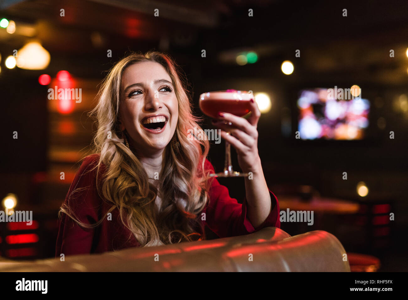 A cheerful young blonde woman in a bar, holding a pink cocktail Stock Photo