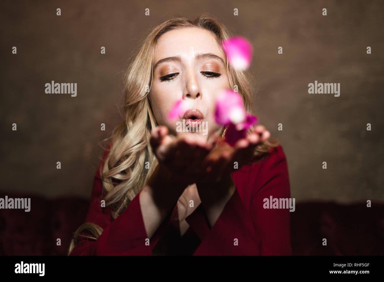 A young blonde woman blowing a kiss of pink rose petals towards the camera Stock Photo