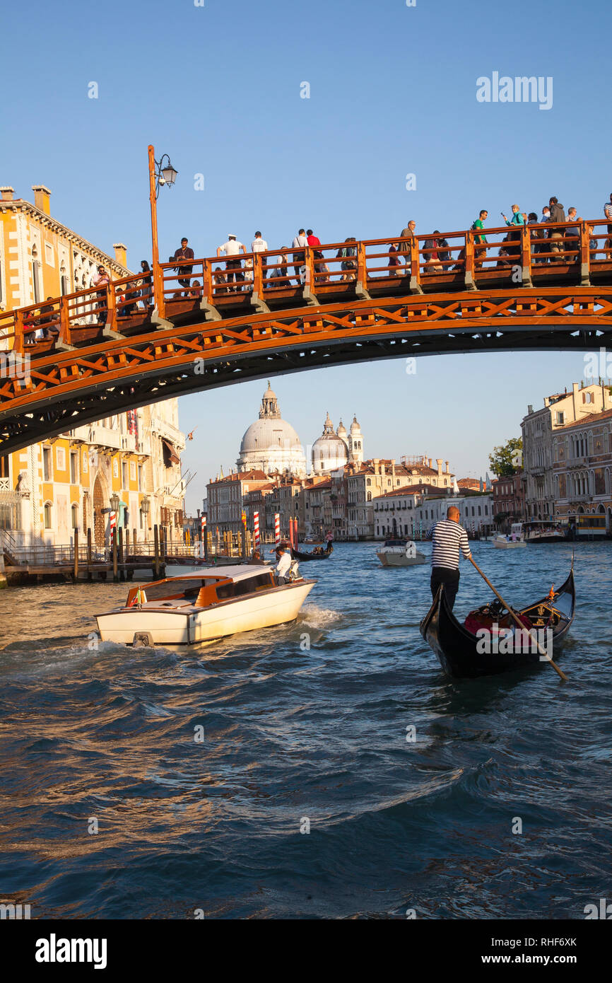 Accademia Bridge and Basilica di Santa Maria della Salute at sunset, Grand Canal, Venice, Veneto, Italy with gondola and water taxi passing under the  Stock Photo