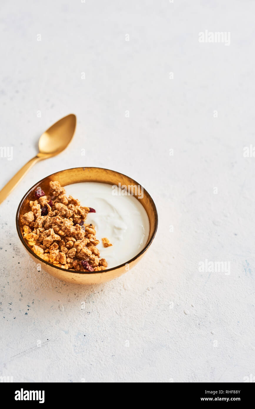 Healthy breakfast. Muesli with Greek yoghurt and honey in golden bowl with golden spoon on white abstract background. Top view. Copy space for text. Stock Photo