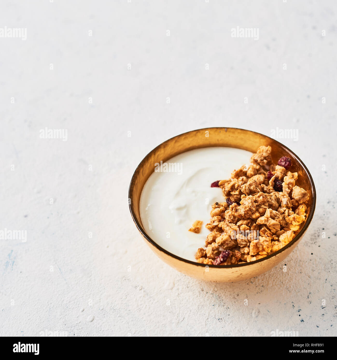Healthy breakfast. Muesli with yogurt and honey in golden bowl on white abstract background. Top view. Square crop. Copy space for text. Stock Photo