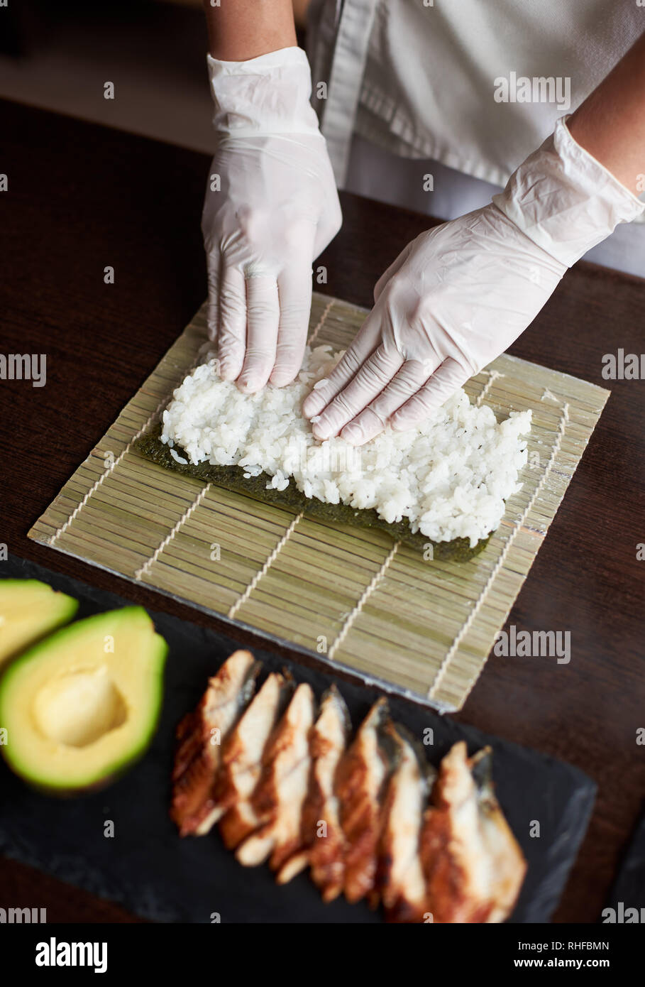 https://c8.alamy.com/comp/RHFBMN/close-up-view-of-process-of-preparing-rolling-sushi-nori-and-white-rice-on-bamboo-mat-chefs-hands-touch-rice-chef-starts-cooking-sushi-eel-and-avocado-RHFBMN.jpg